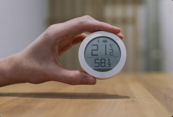 Mão segurando higrômetro digital que mede temperatura e umidade relativa do ar em incubadora de ovos.